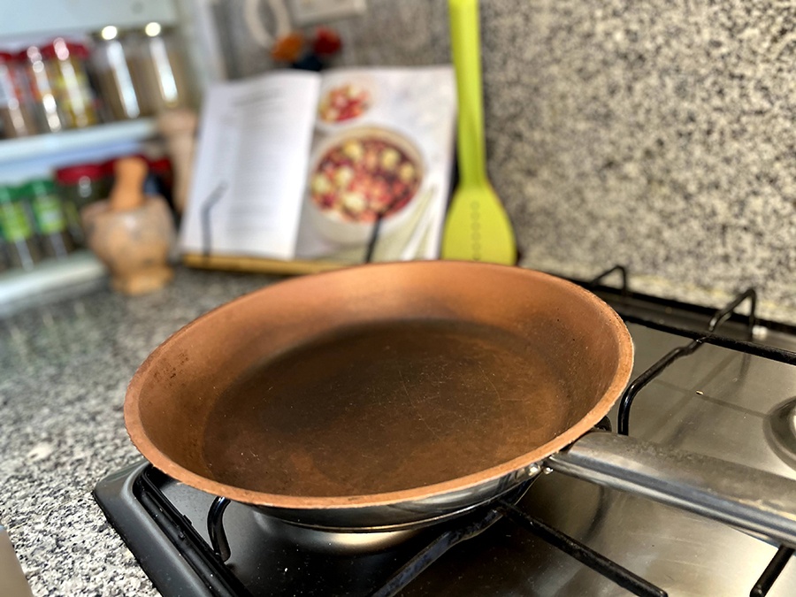 A discoloured copper frying pan with a scratched surface