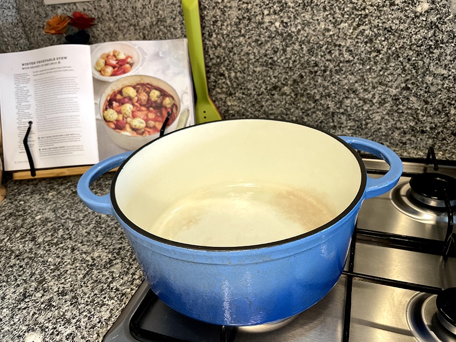 A blue enamel-coated cat iron pan in front of a cookbook